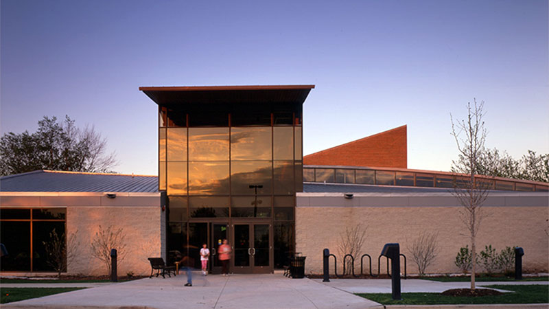 Modern building with a large glass entrance, lit by evening light. Two people stand near the entrance.