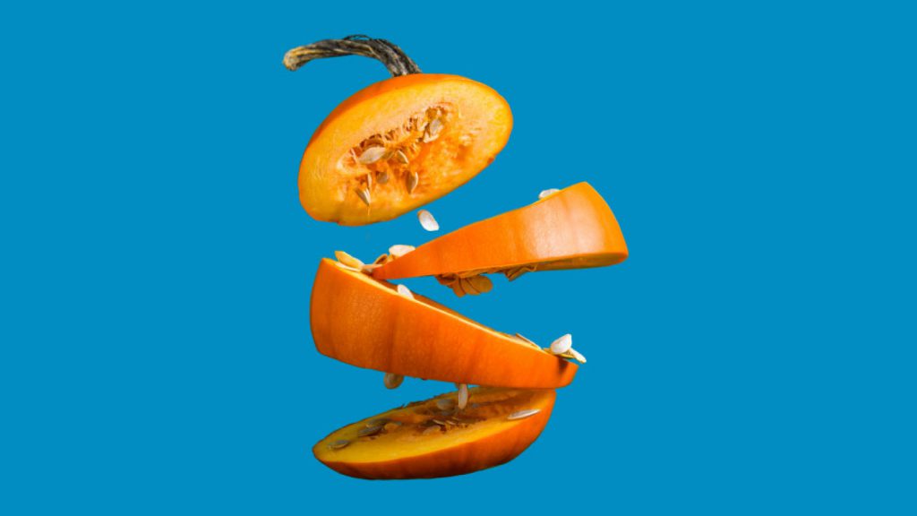 A levitating sliced pumpkin with seeds and stem against a blue background.