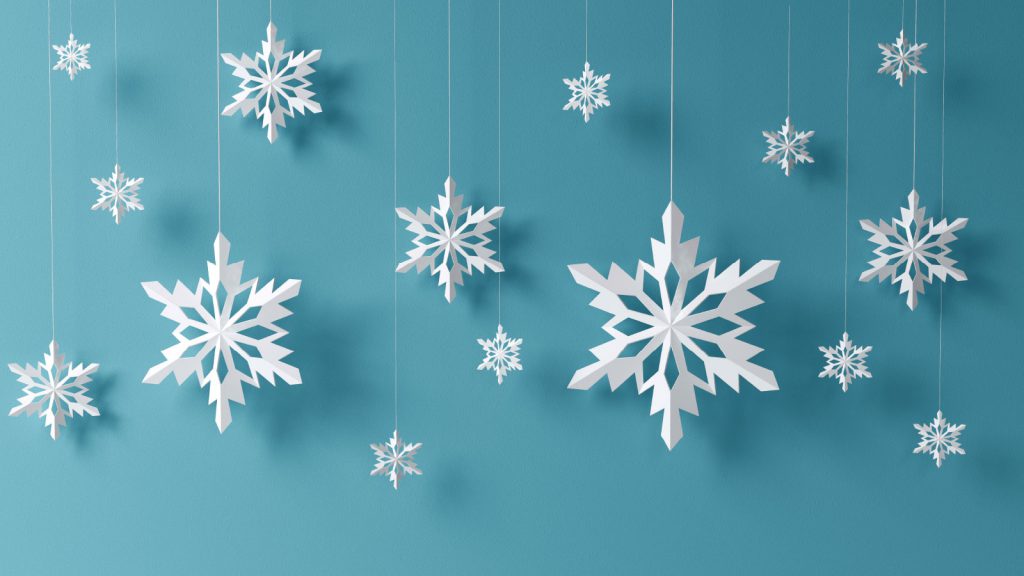 White paper snowflakes hanging on strings with a blue background, creating a holiday-themed decoration.