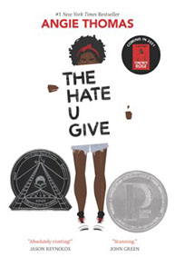 Book cover of "The Hate U Give" by Angie Thomas featuring a girl holding up a sign and two award emblems at the bottom.