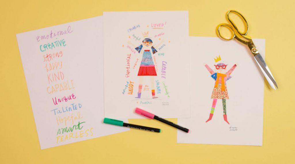 Two colorful drawings, a list of positive adjectives, markers, and a pair of scissors on a yellow surface.