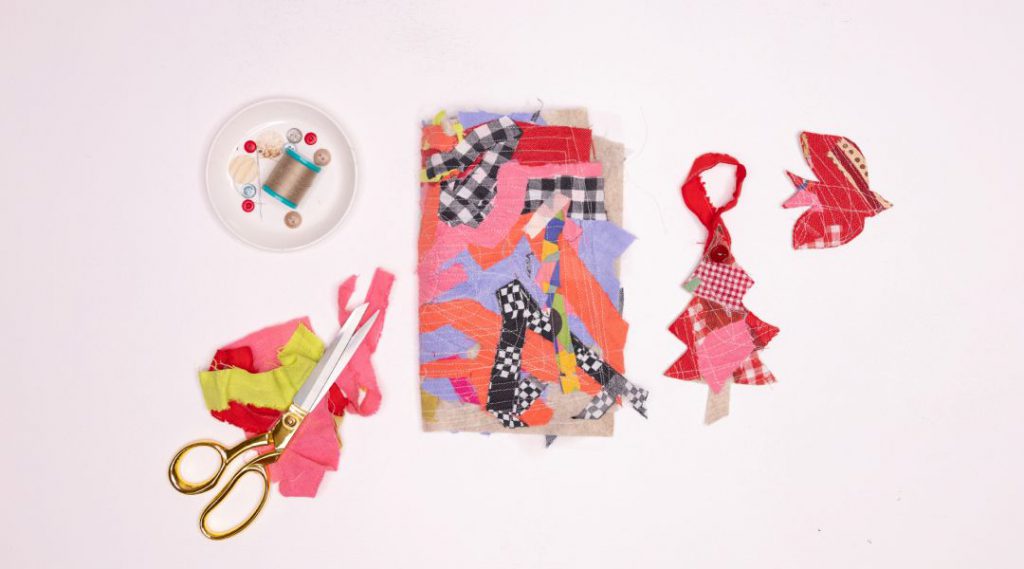 Scissors, thread, and fabric scraps arranged around cut-out shapes of a bird and Christmas tree on a white background.