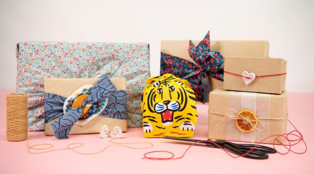 A variety of wrapped gifts with decorative bows, patterned paper, and twine, along with scissors and buttons on a table.