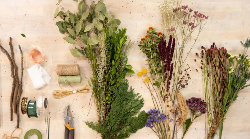 A variety of dried flowers, garden tools, and crafting supplies arranged on a wooden surface.
