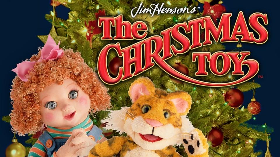 Doll and tiger puppet in front of a Christmas tree, with "The Christmas Toy" text in red above them.