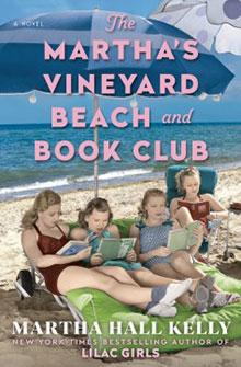 Four girls read books under umbrellas on a sandy beach, with the ocean and sky in the background.