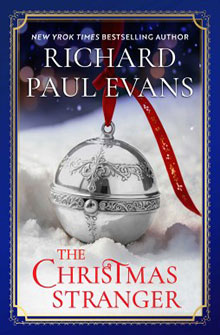 A silver ornament on snow with the book title "The Christmas Stranger" by Richard Paul Evans.