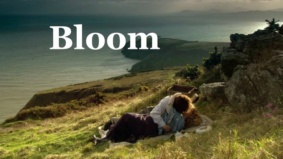 Couple embracing on a grassy cliff overlooking the sea, with "Bloom" written above.