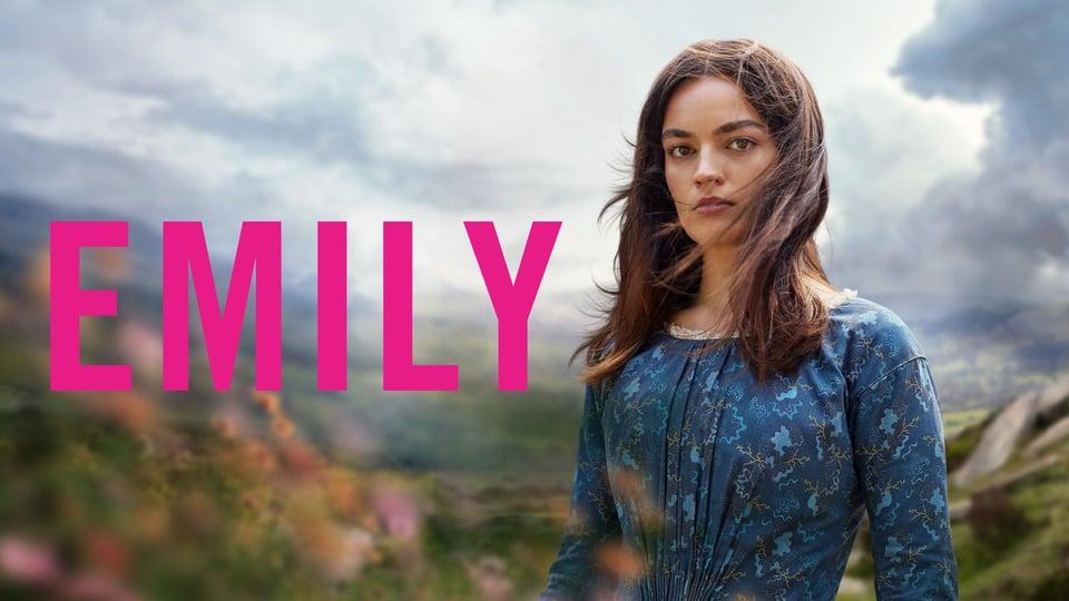 A woman in a blue dress stands outdoors with "EMILY" in pink text beside her. Cloudy sky and hills in the background.