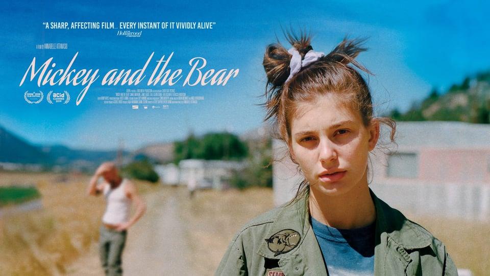 Woman with a top bun stands on a rural road; blurred figure in the background. Text: "Mickey and the Bear.