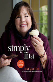 Woman in a maroon wrap smiles, holding a cupcake and a cookie; text reads “simply ina” and “ina garten.”.