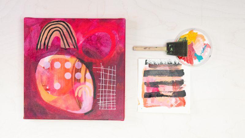 Abstract painting with bold pinks, reds, and geometric patterns next to a paintbrush and palette.