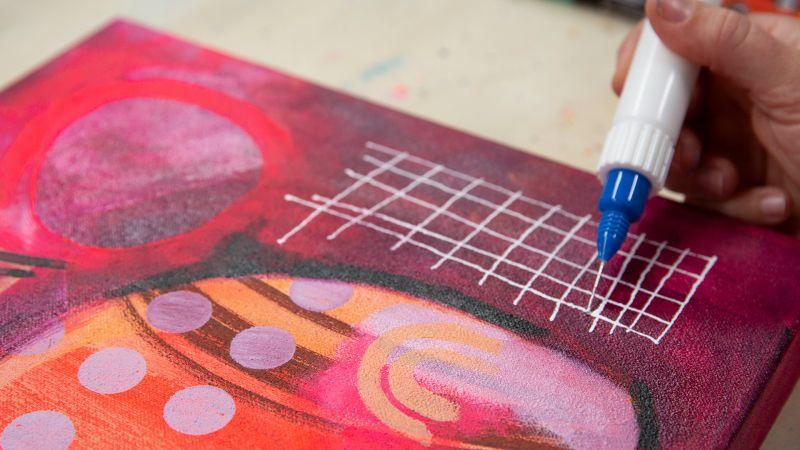 Hand drawing white grid on colorful abstract painting with a blue paint pen.