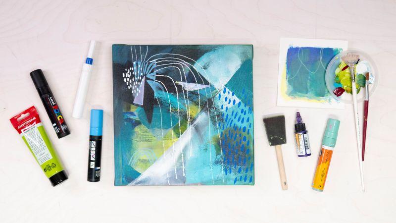 Abstract painting with blue and green tones, surrounded by art supplies on a white surface.