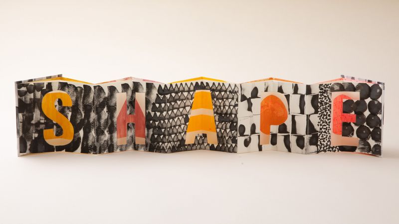 Accordion-folded paper art displays the word "SHAPE" with each letter decorated in bold patterns and varying textures.