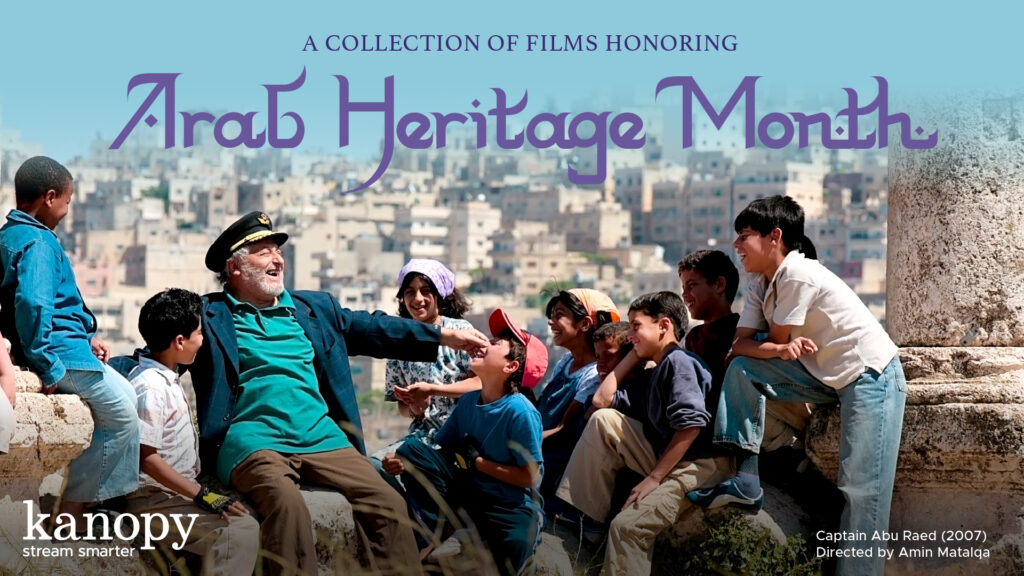 A smiling man in a captain’s hat sits with a group of smiling children outdoors, promoting Arab Heritage Month.