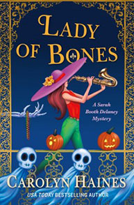 Book cover of "Lady of Bones" by Carolyn Haines, featuring a woman in a hat playing a saxophone, pumpkins, and skulls.