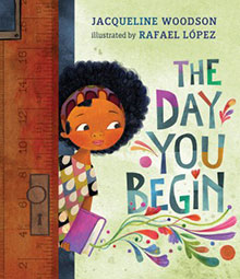 Book cover of "The Day You Begin" by Jacqueline Woodson, illustrated by Rafael López, featuring a girl holding a book.