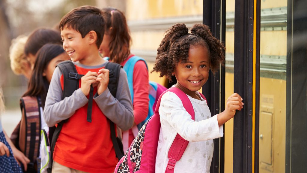 Children with backpacks smiling and boarding a yellow school bus.