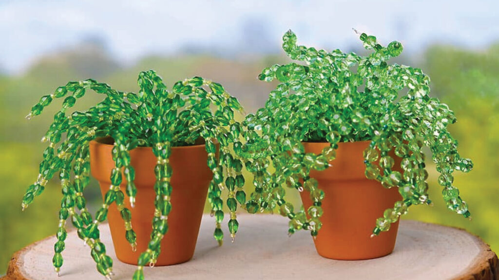 Two small clay pots holding artificial green plants made from twisted beads, sitting on a wooden surface.