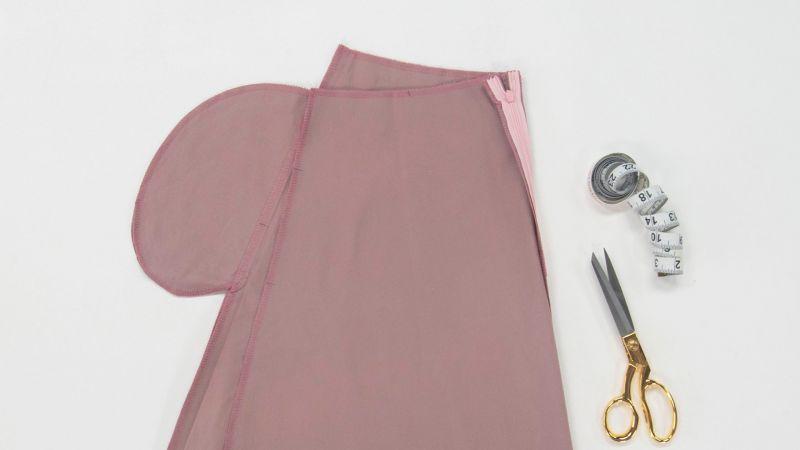 Pink fabric laid out with a measuring tape, scissors, and thread spool on a white surface.