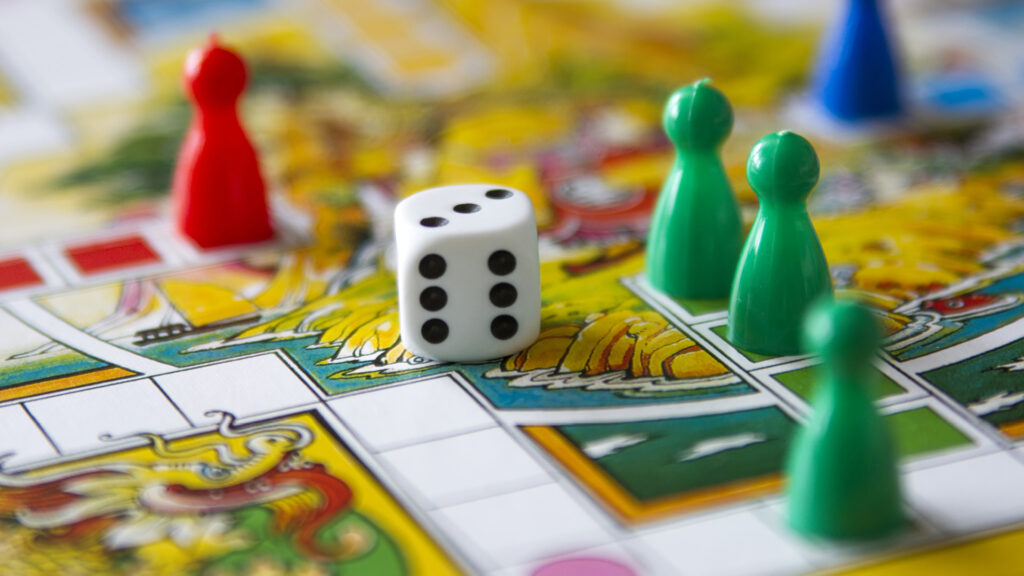 Close-up of a colorful board game with a die and green, red, and blue playing pieces on a dragon-themed board.