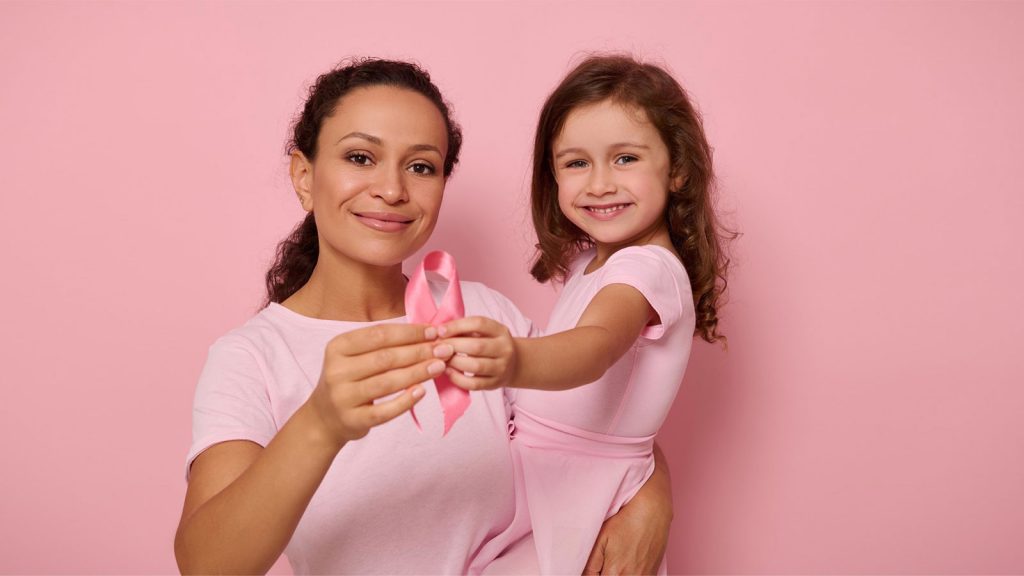 A woman and a young girl in pink shirts hold a pink ribbon, symbolizing breast cancer awareness, against a pink background.