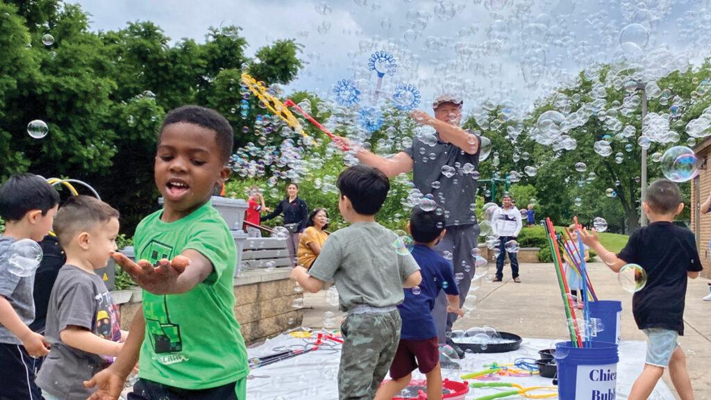 Children play with bubbles outdoors on a sunny day, chasing and popping bubbles with joy.