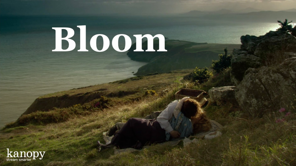 A couple lies together on a grassy cliffside overlooking the sea, with the word "Bloom" in large text above.