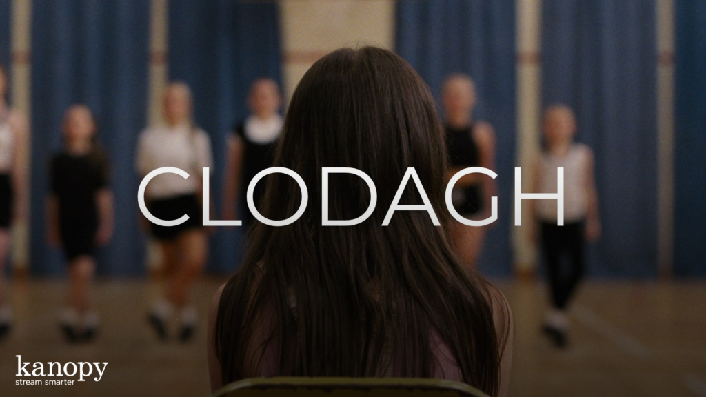 A girl with long brown hair faces dancers on stage; the word "CLODAGH" appears across the image.