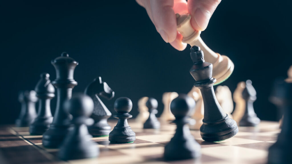 A hand moves a white chess piece, capturing a black king on a chessboard during a game.