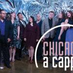 A group of people stand joyfully together in formal attire with a "Chicago a cappella" sign in front.