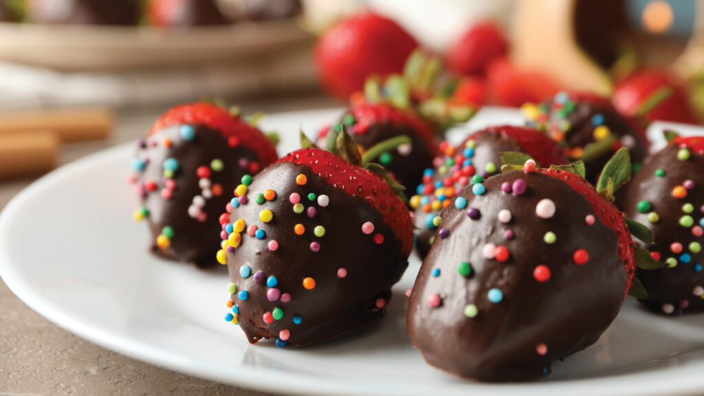 Chocolate-covered strawberries with colorful sprinkles on a white plate.