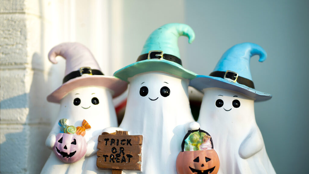 Three cute ghost figurines with colorful witch hats hold jack-o’-lanterns and a “Trick or Treat” sign.