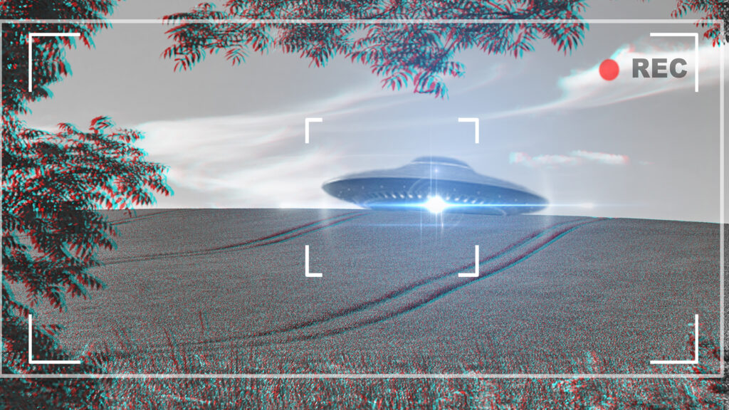 A grainy video frame shows a flying saucer hovering above a grassy hill under cloudy skies.