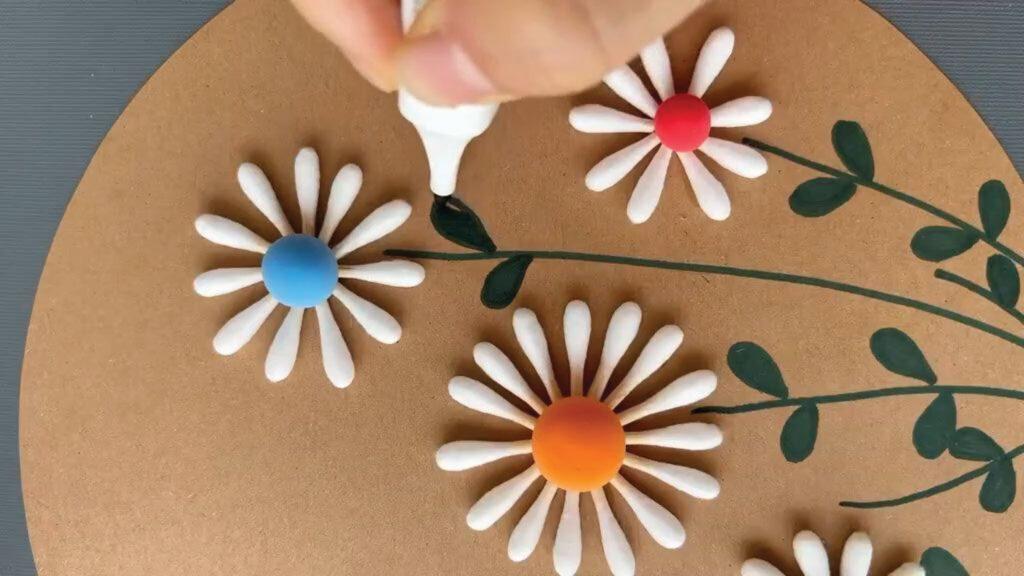 Hand adding details to clay flowers with colorful centers on a brown background.