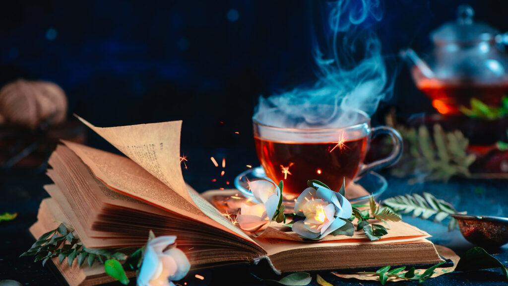 A steaming cup of tea with an open book and flowers, creating a cozy and magical atmosphere.