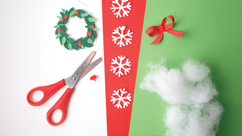 Red scissors, paper wreath, snowflakes, ribbon, and cotton on red, green, and white background for crafts.