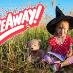 A cheerful girl in a witch hat sits in a grassy field with a teddy bear, next to the word "Giveaway!" in bold letters.