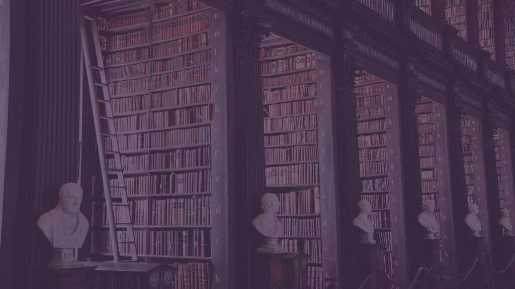 A dimly lit library with tall shelves of books, a ladder, and busts of notable figures lining the path.