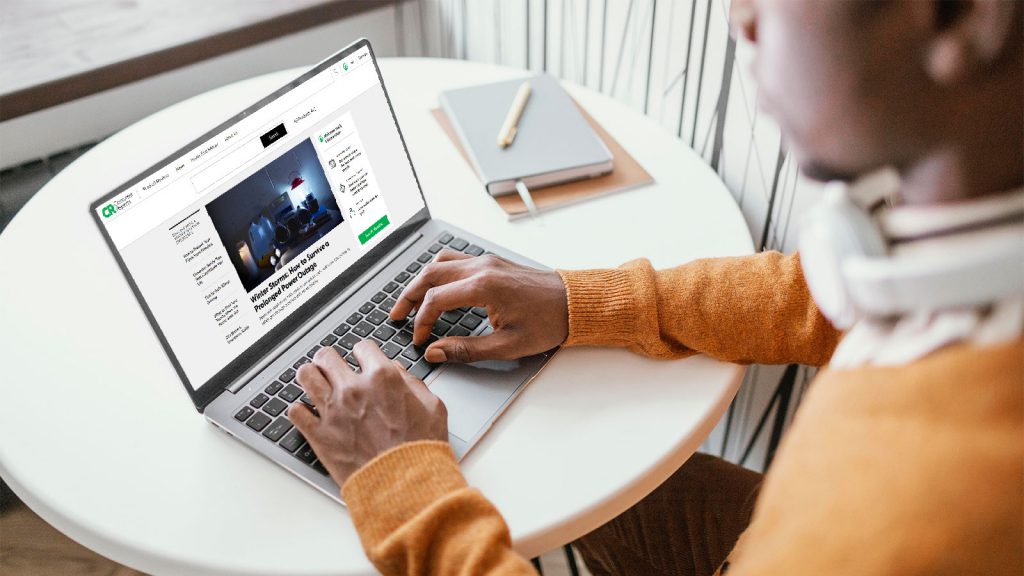 Person typing on a laptop, browsing a news article at a white round table with a notebook and pencil in the background.