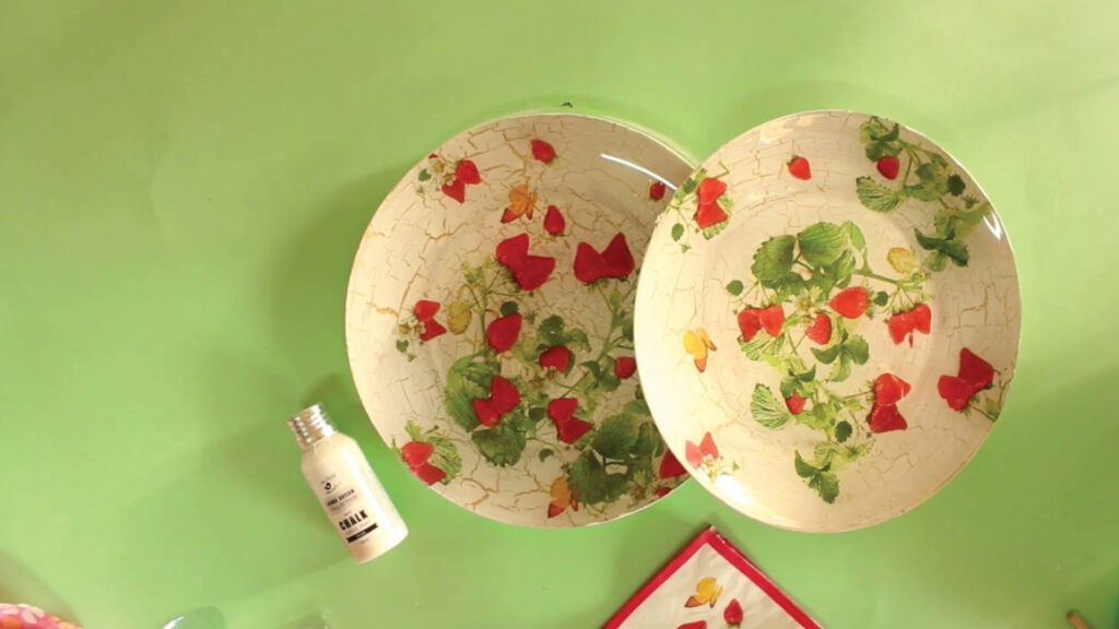 Two decorative plates with red flowers and green leaves on a light green surface, next to a small white bottle.