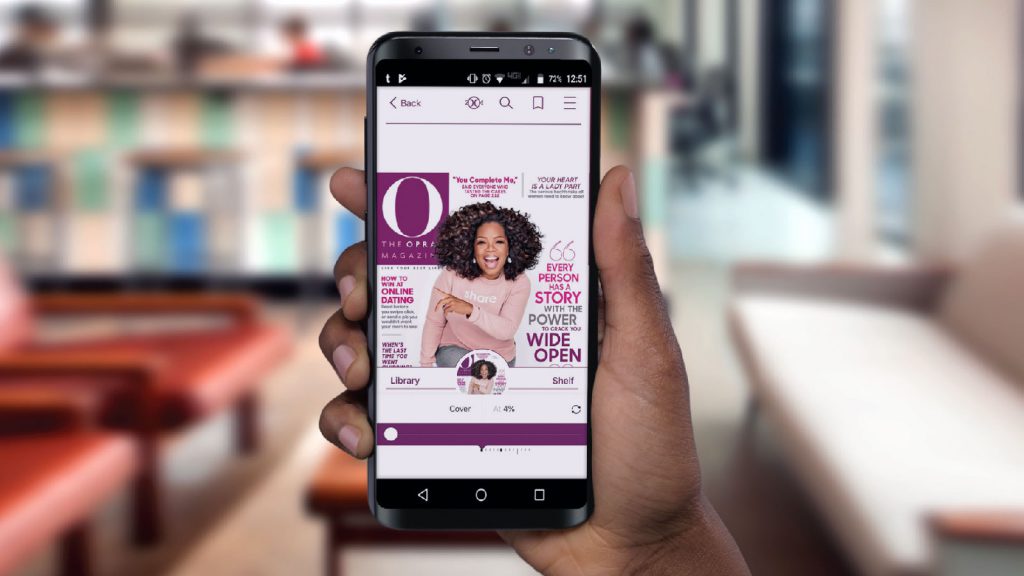 A person holds a smartphone displaying a digital magazine cover with a woman in a light top and the title "O, The Oprah Magazine.