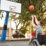 Man in a wheelchair shooting a basketball towards a hoop on an outdoor court.