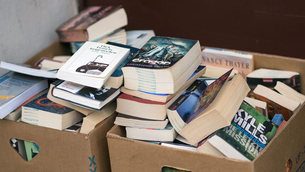 A pile of books, some stacked and some scattered, in two cardboard boxes.