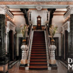 Grand marble staircase with ornate columns, statues, and the Driehaus Museum logo in the bottom right corner.