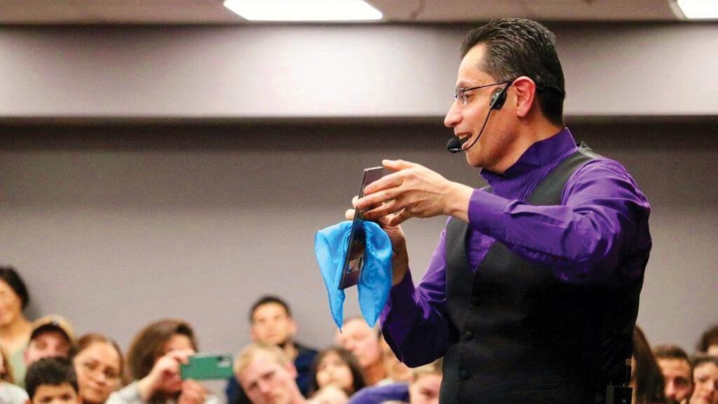 A speaker in a purple shirt and headset demonstrates with a cloth and phone to a seated audience.