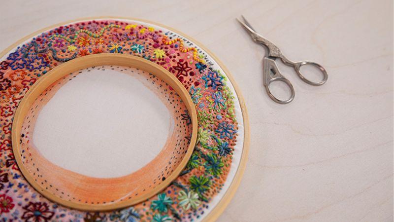 Embroidery hoop with colorful floral patterns next to scissors on a light surface.