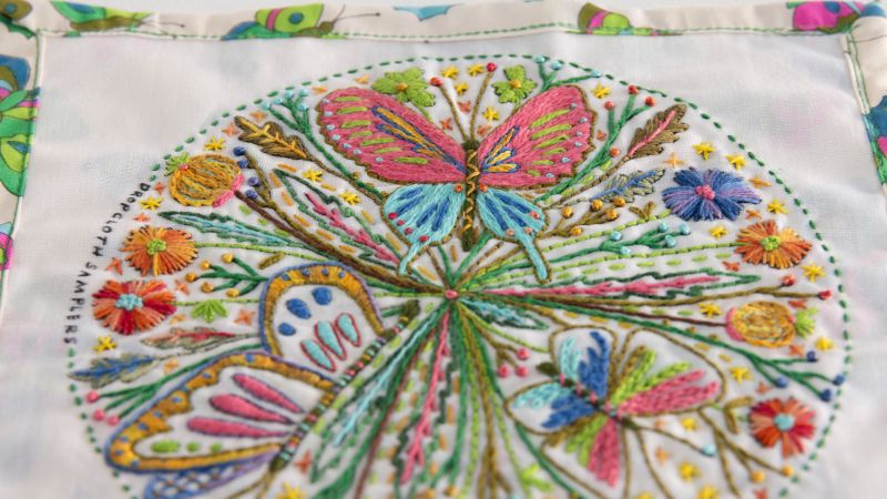 Colorful embroidery of butterflies and flowers within a circular frame on white fabric with a vibrant border.