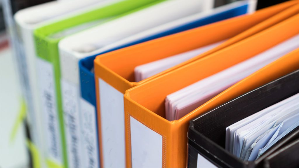 Close-up of brightly colored binders on a shelf, with some filled with paper.